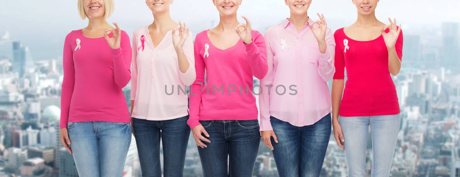 healthcare, people, gesture and medicine concept - close up of smiling women in blank shirts with pink breast cancer awareness ribbons showing ok sign over city background