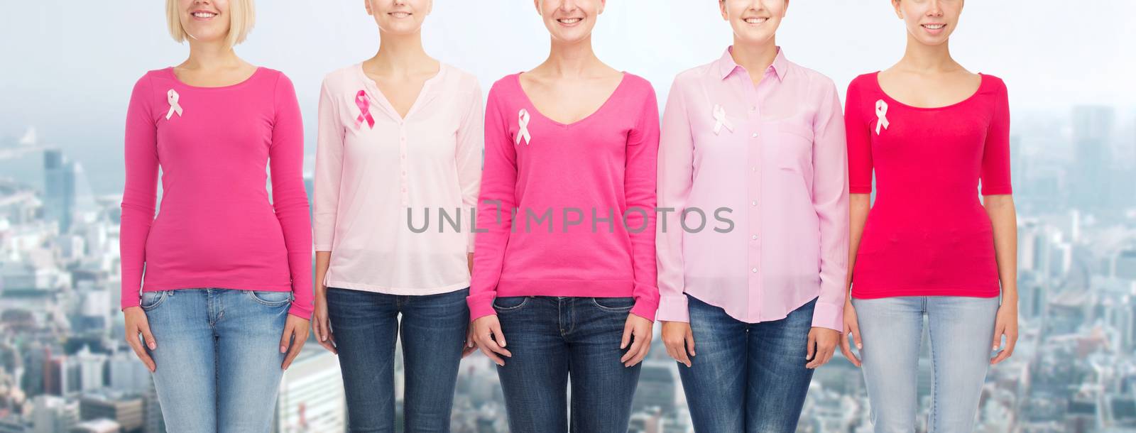 healthcare, people and medicine concept - close up of smiling women in blank shirts with pink breast cancer awareness ribbons over city background