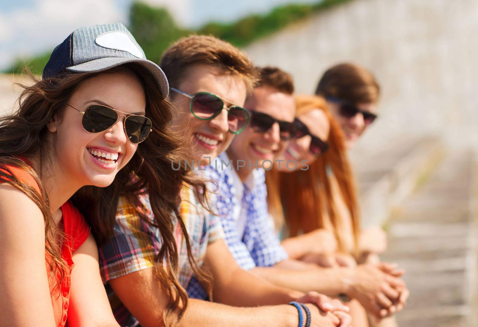 friendship, leisure, summer and people concept - close up of smiling friends sitting on city street