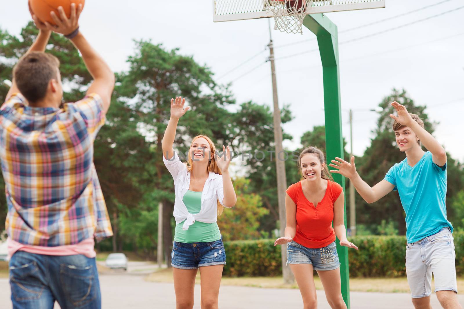 summer vacation, holidays, games and friendship concept - group of smiling teenagers playing basketball outdoors