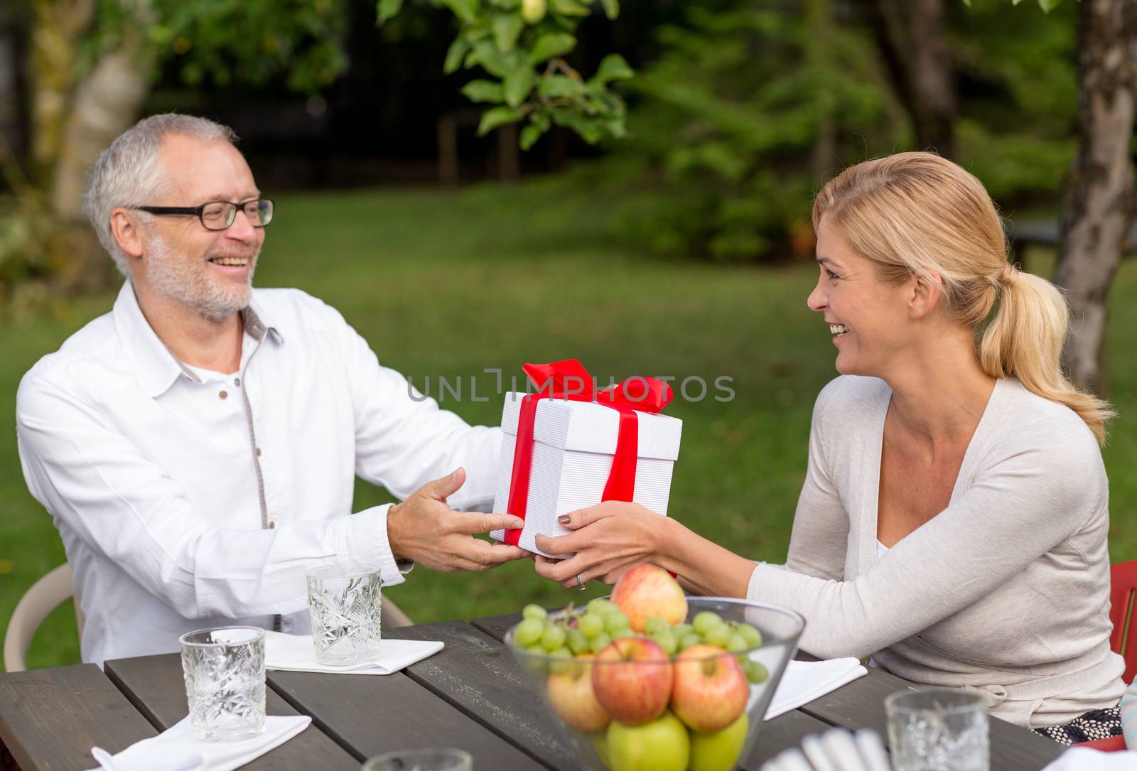 family, happiness, generation, home and people concept - happy family with gift box having holiday dinner outdoors