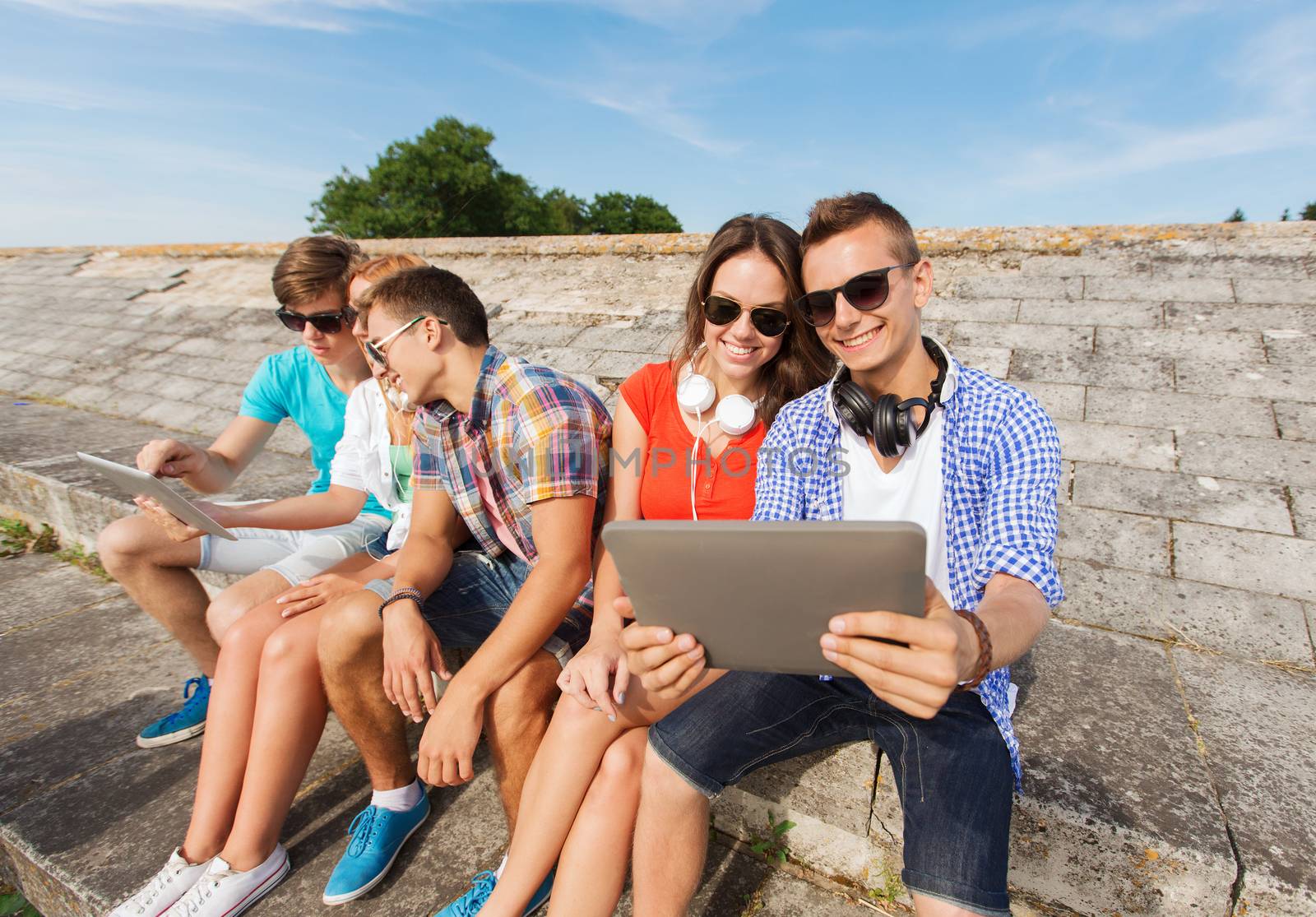 group of smiling friends with tablet pc outdoors by dolgachov