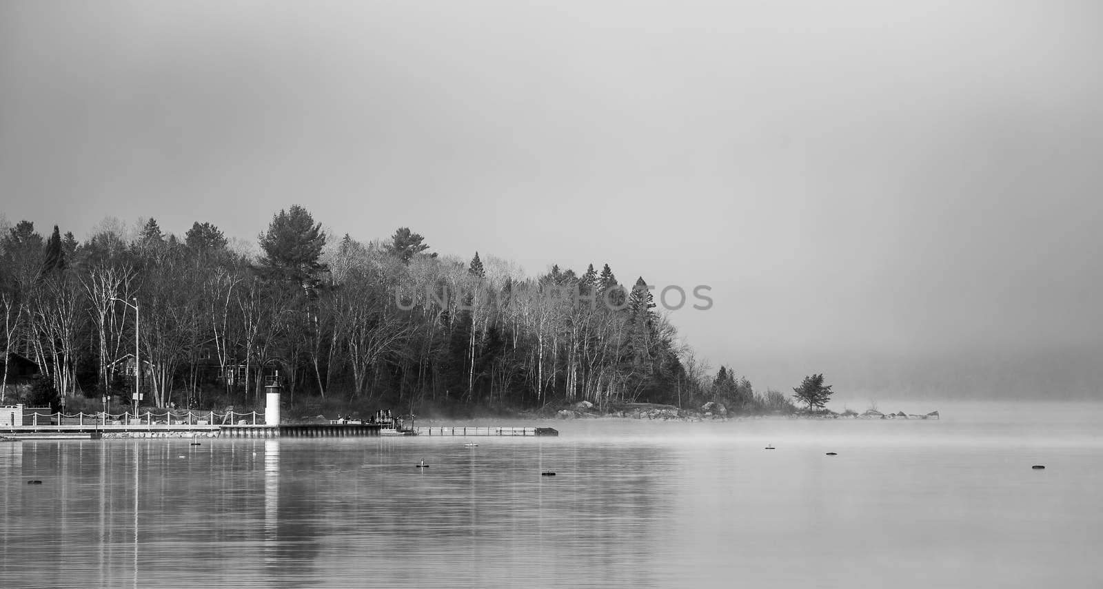 Heavy blanket of fog lifting off the Ottawa River revealing a small peninsular forest and lighthouse, Ontario Canada.