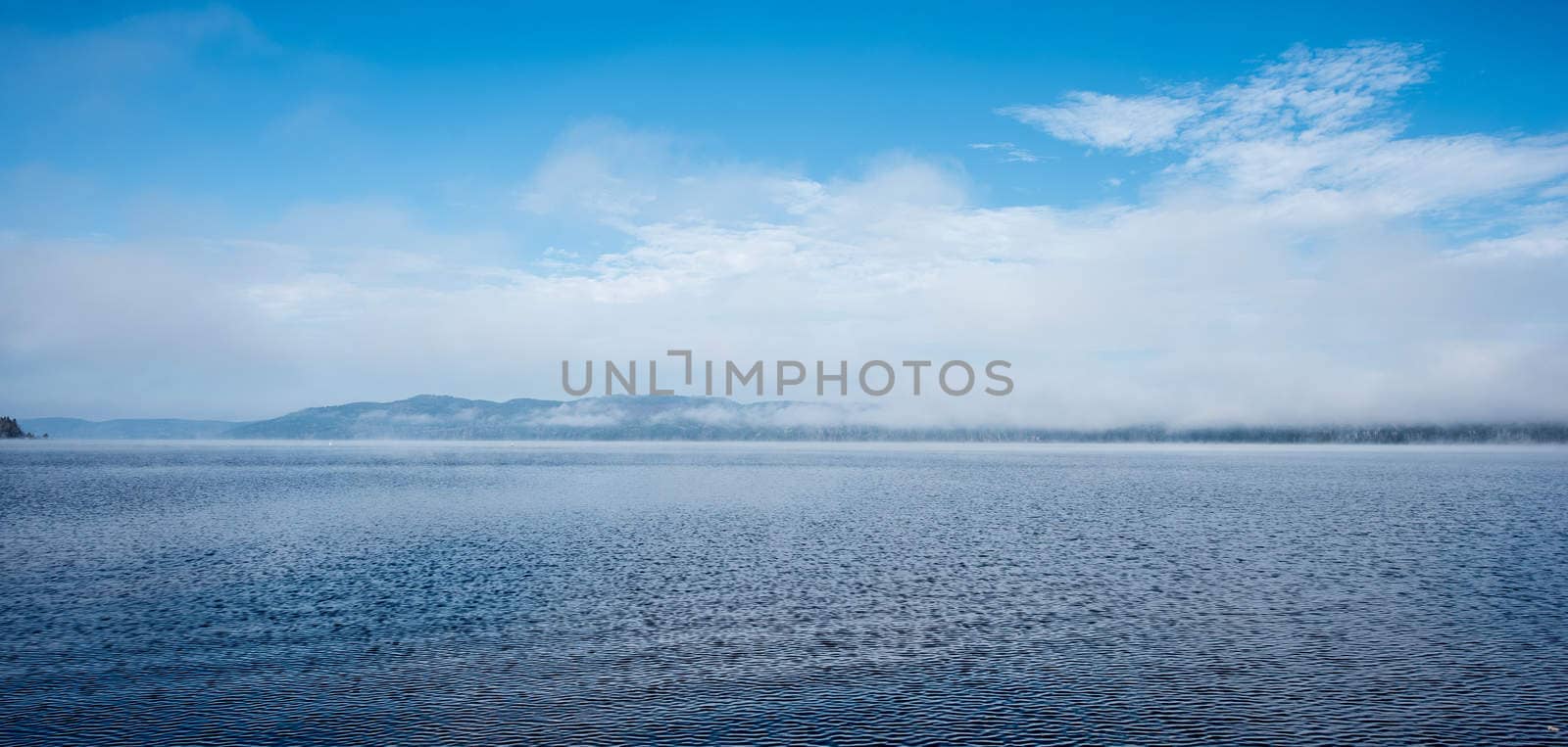 Fog rising from blue water into sky  - Panoramic fog lifting off the Ottawa River in late morning with Laurentian Hills and mountains -