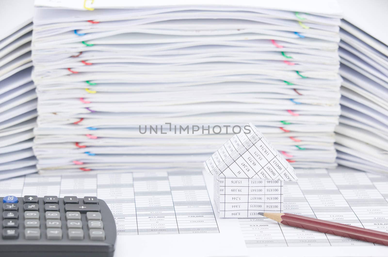 House and brown pencil with calculator on finance account have blur pile of paperwork as background.