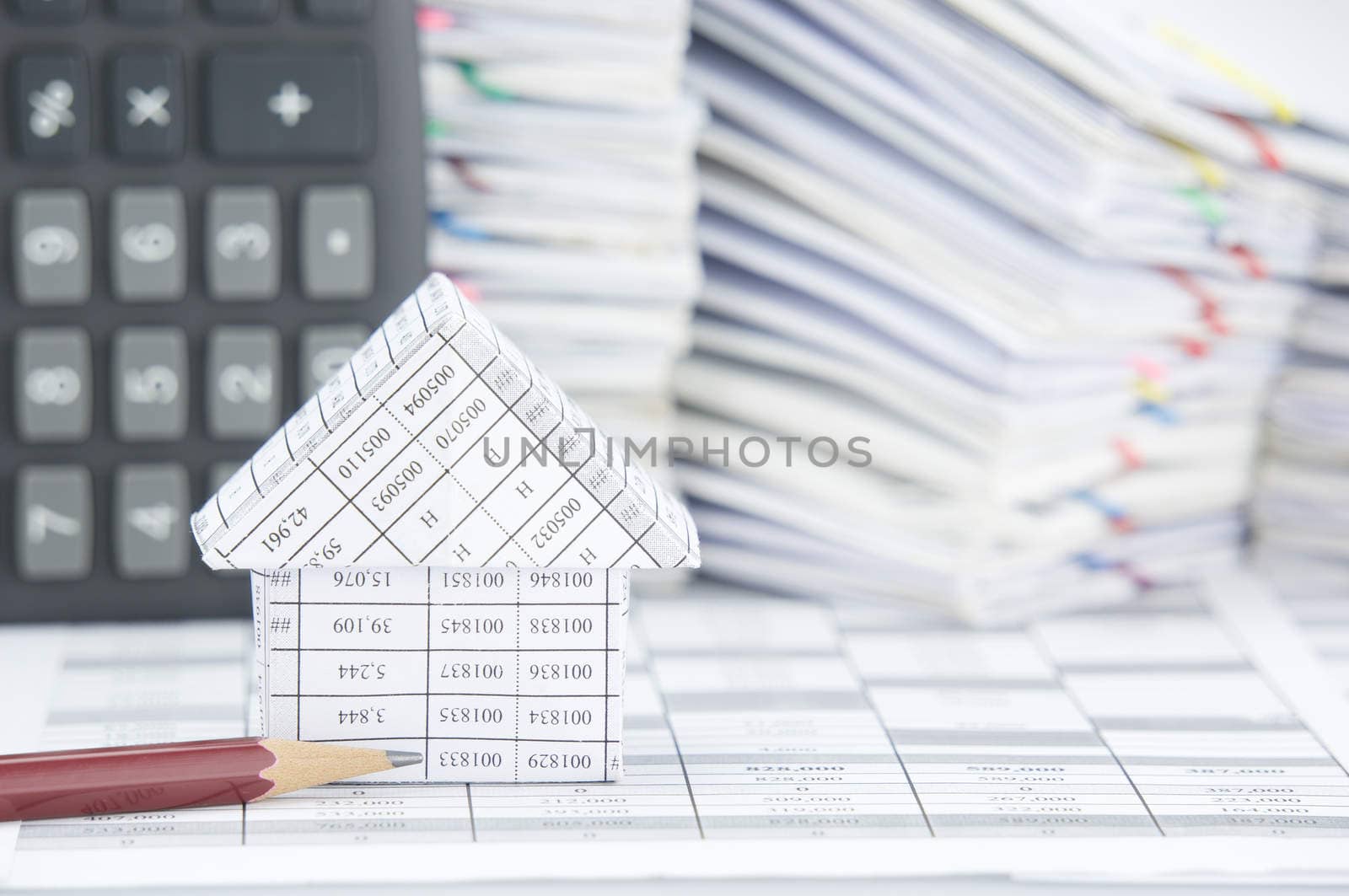 Brown pencil and house on finance account have blur calculator and pile of paperwork as background.