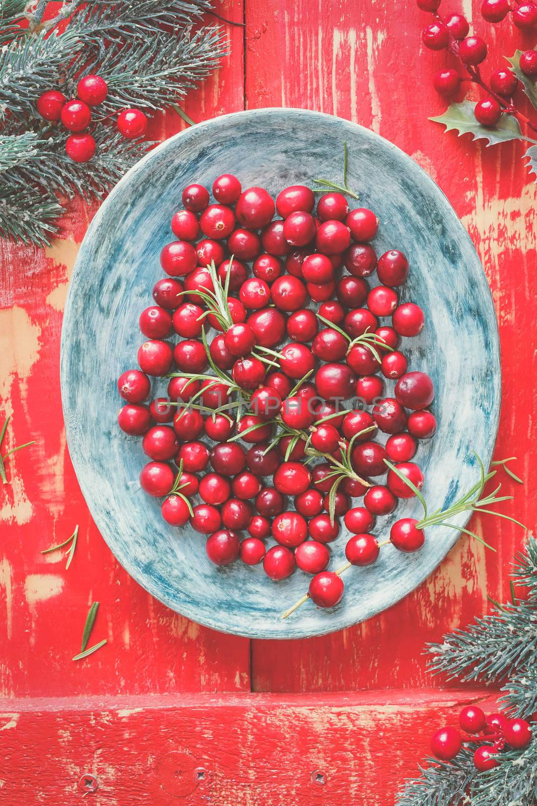 Fresh red Cranberries on a plate, painted wooden background. Top view, vintage toned