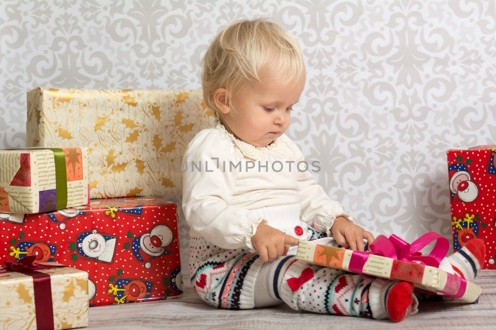 An adorable baby girl concentrate when holding a wrapped Christmas gift