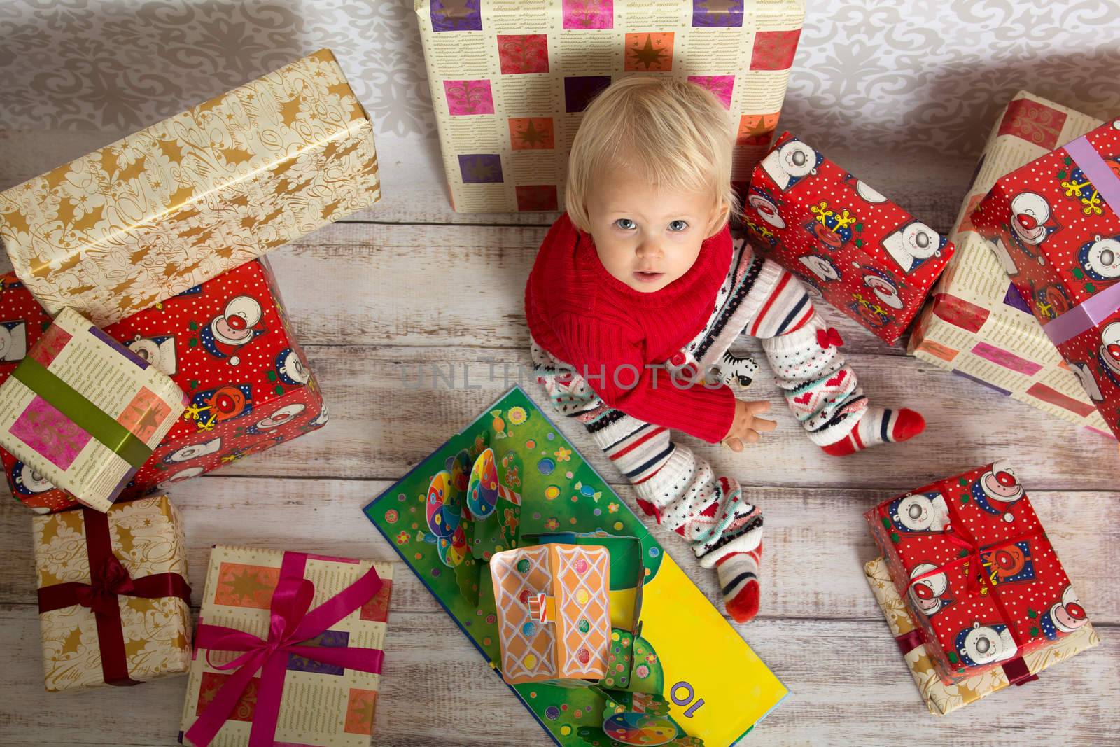 Dressed festively girl with stacks of present boxes around sitting on the floor and looking at the camera