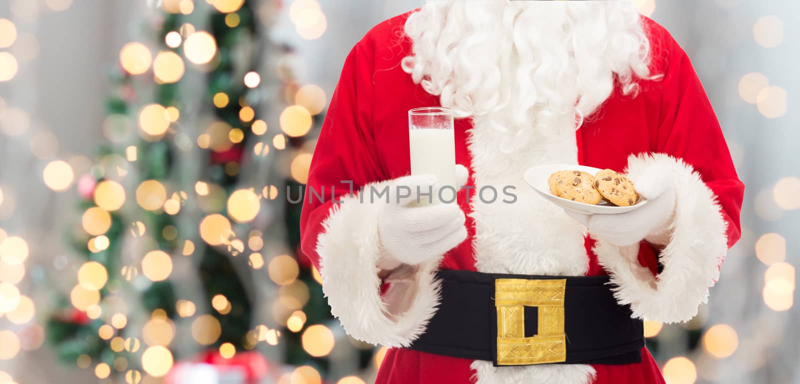 christmas, holidays, food, drink and people concept - close up of santa claus with glass of milk and cookies over tree lights background