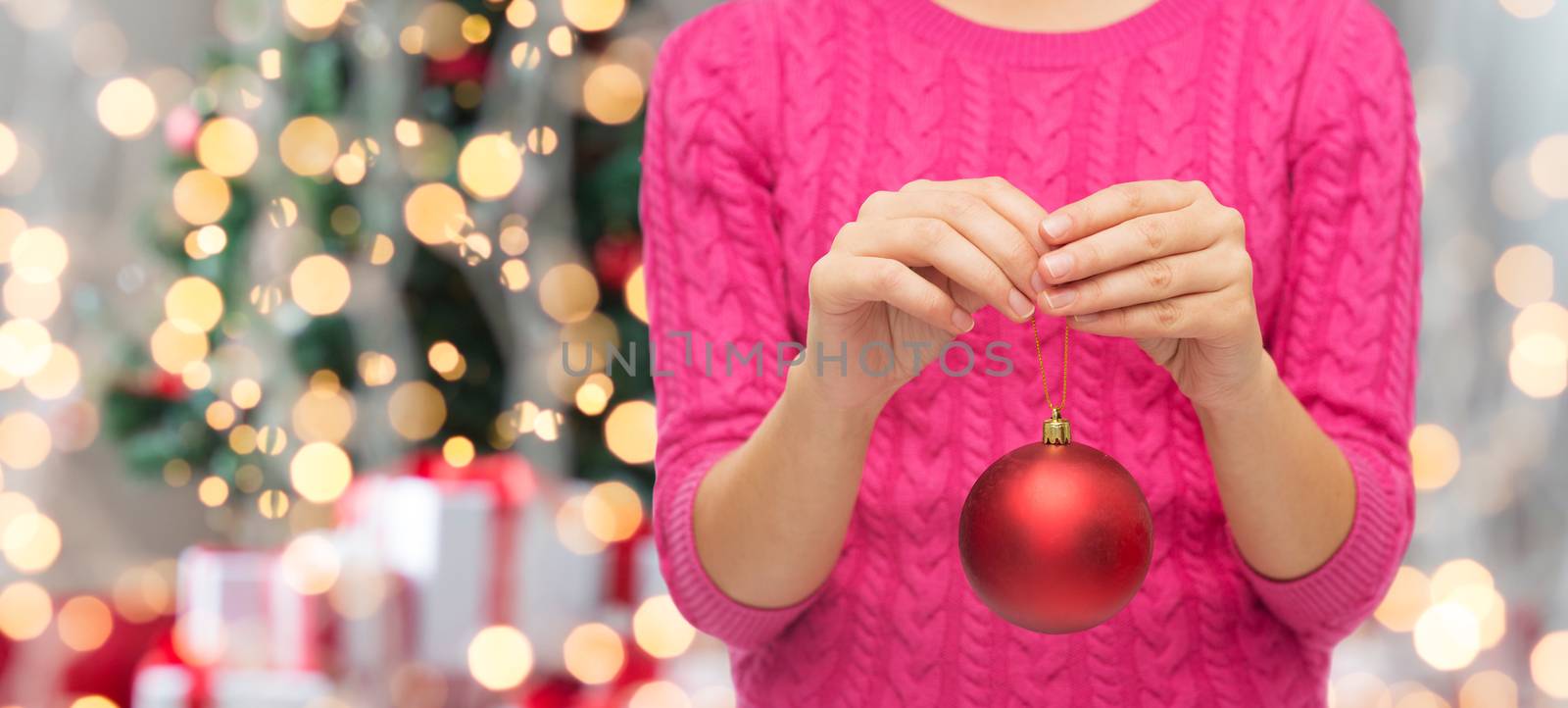 christmas, decoration, holidays and people concept - close up of woman in pink sweater holding christmas ball over tree lights background