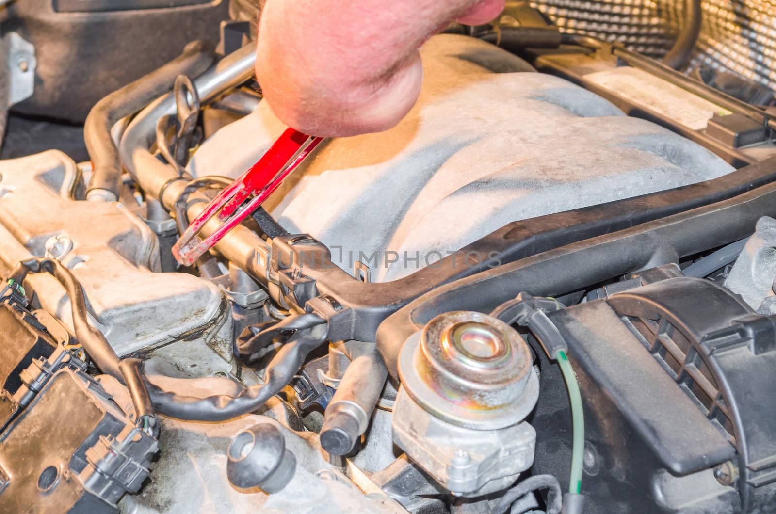 Hand of an auto mechanic in the engine compartment in the car-repair workshop.