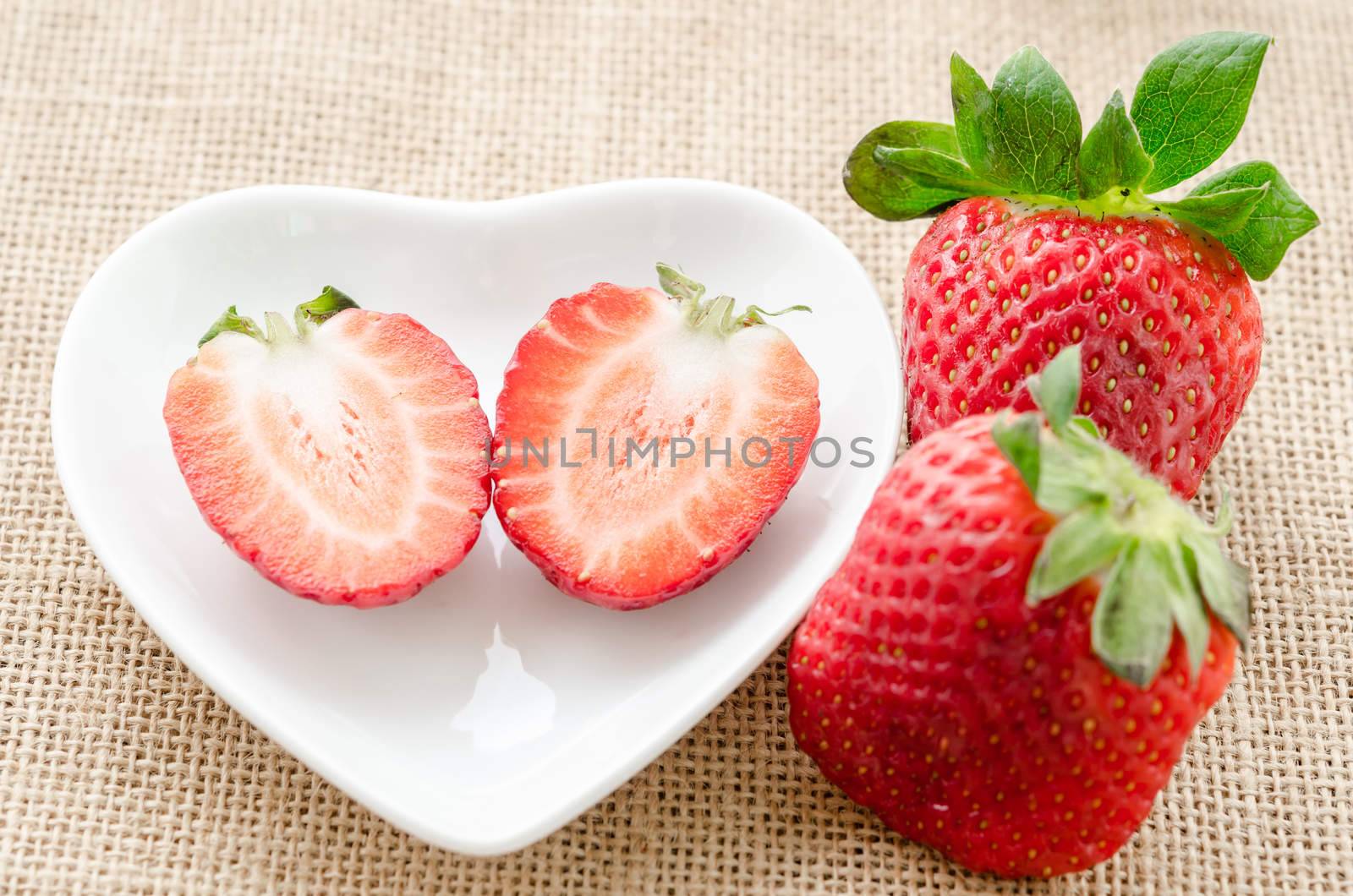 Ripe sweet strawberries in white bowl on sack background.