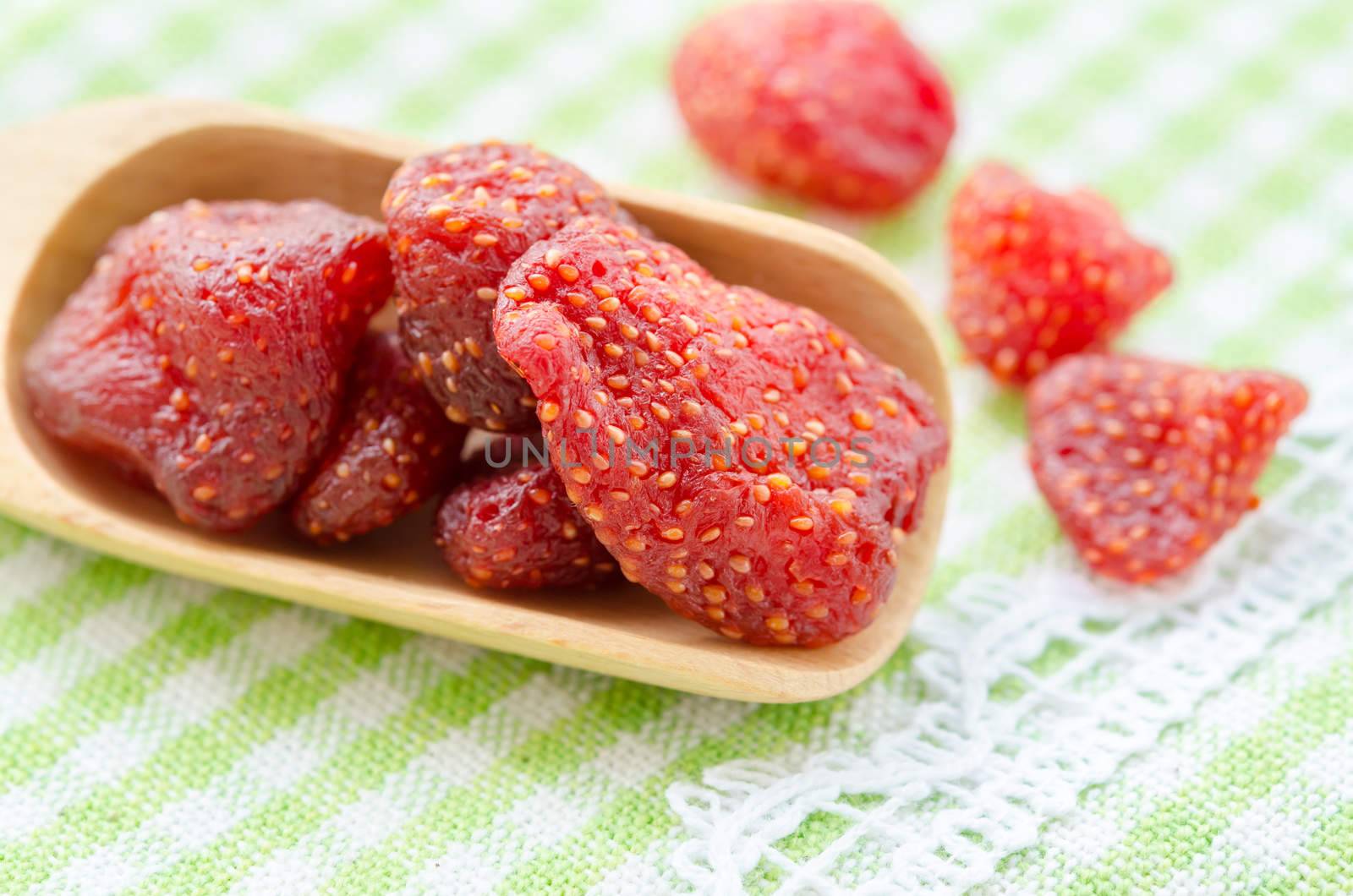 Dried strawberries in wooden spoon on tablecloth.