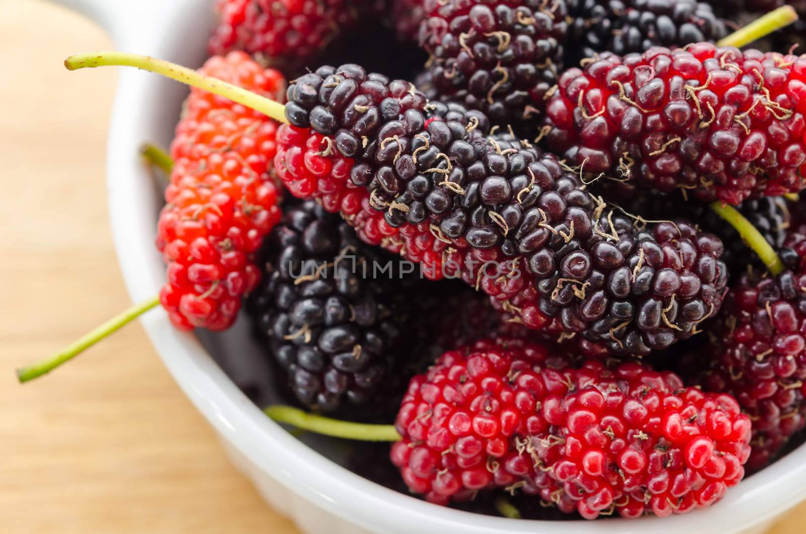 Fresh mulberry in white cup on wood background.