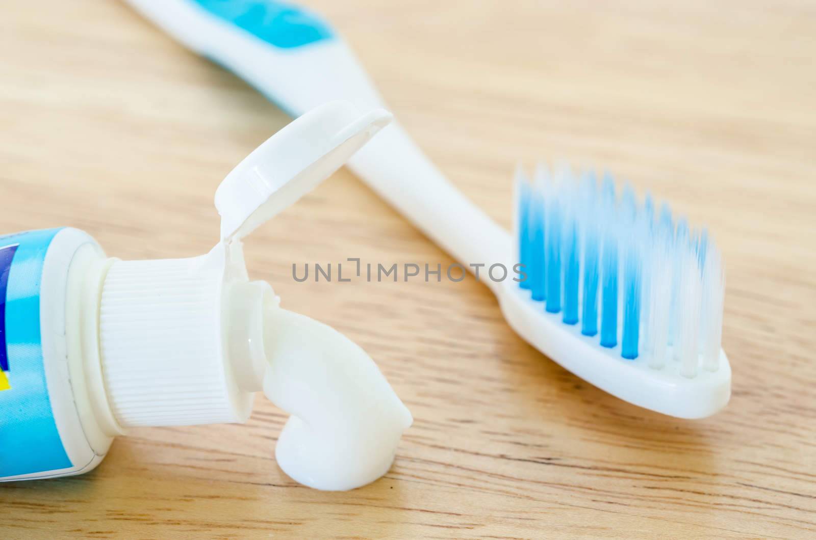 White toothpaste spill out a tube of toothpaste and toothbrush on wooden background.