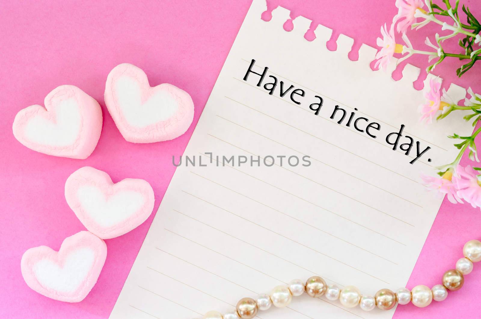 Have a nice day written with sweet heart shape of pink marshmallows with flower on pink background.