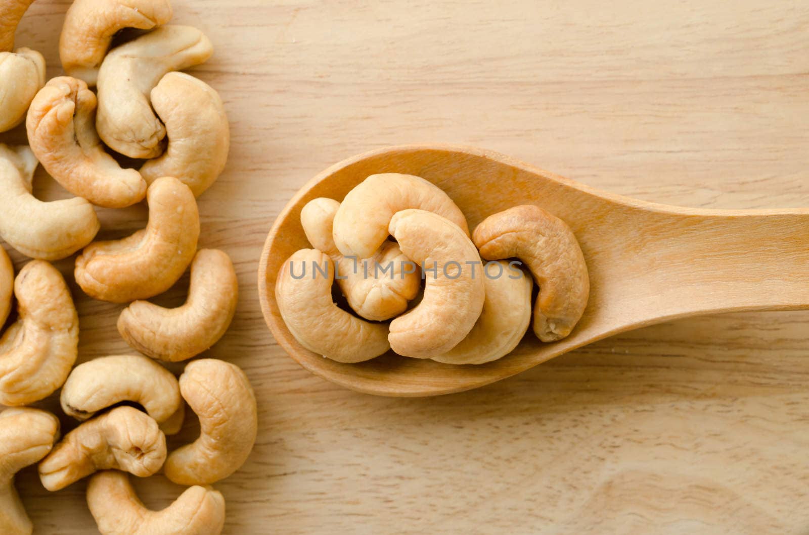 Heap of a roasted cashew nuts in wooden spoon on wood background.
