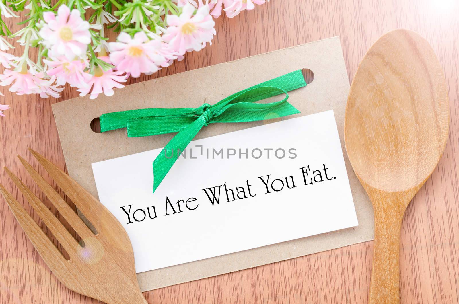 You are what you eat message in paper tag with wooden spoon on wooden background. Healthy concept.