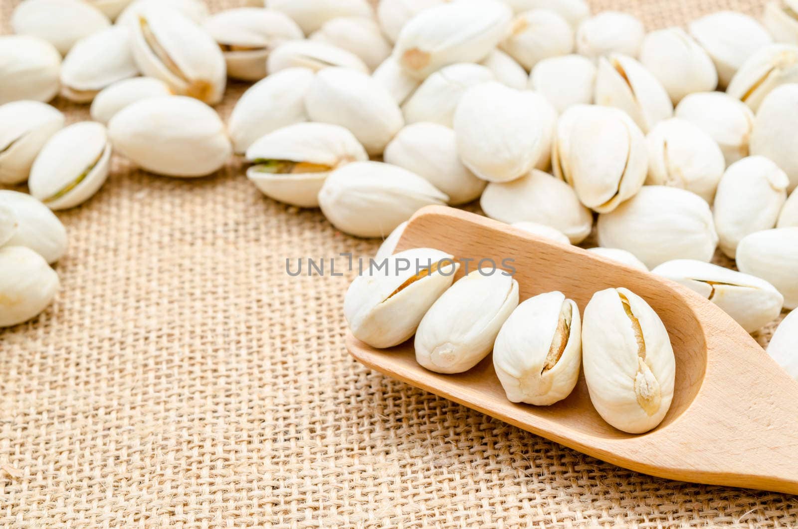 Pistachio in wooden spoon on sack background.