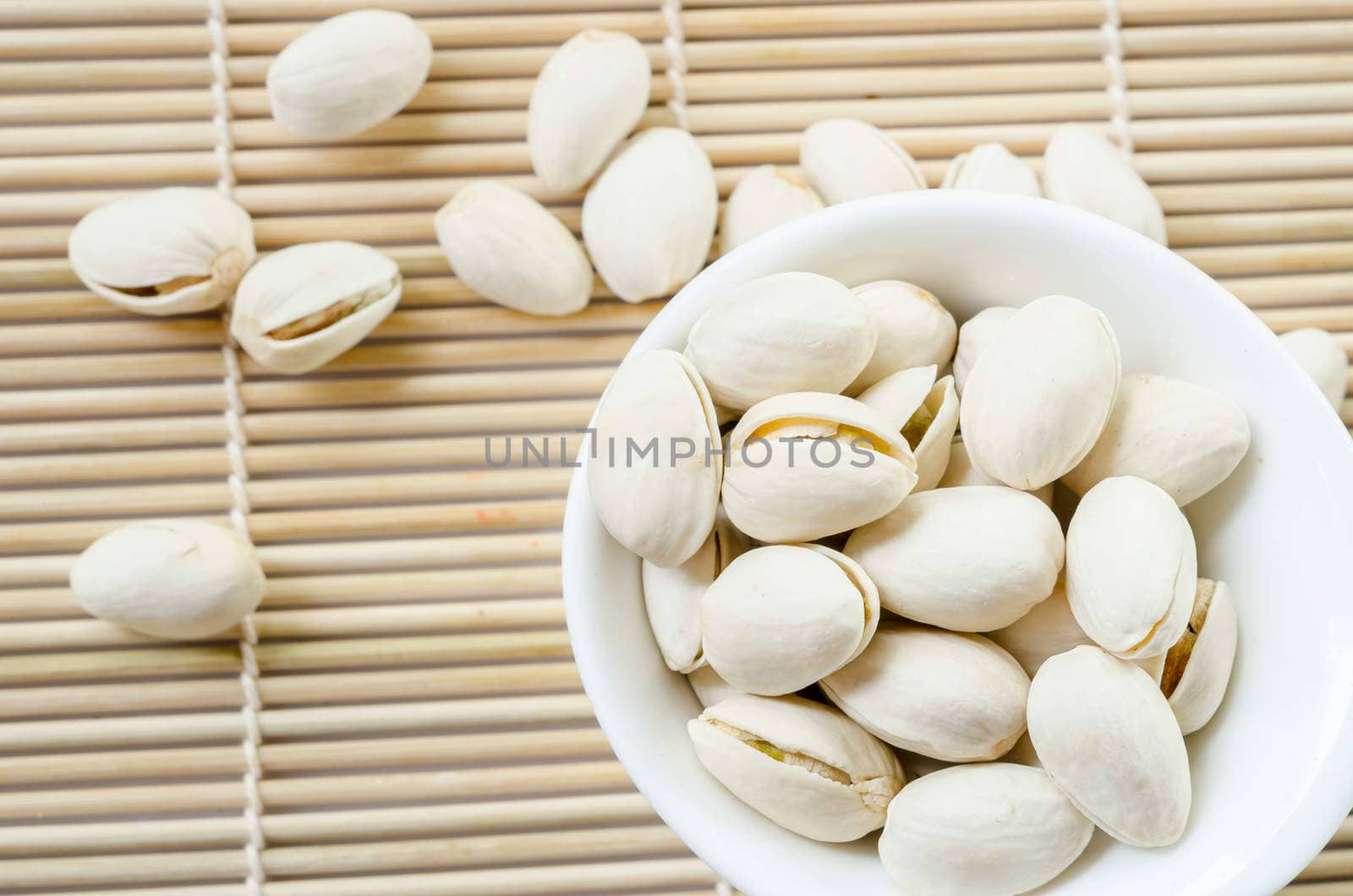 Pistachio in white cup on bamboo mat on white background.