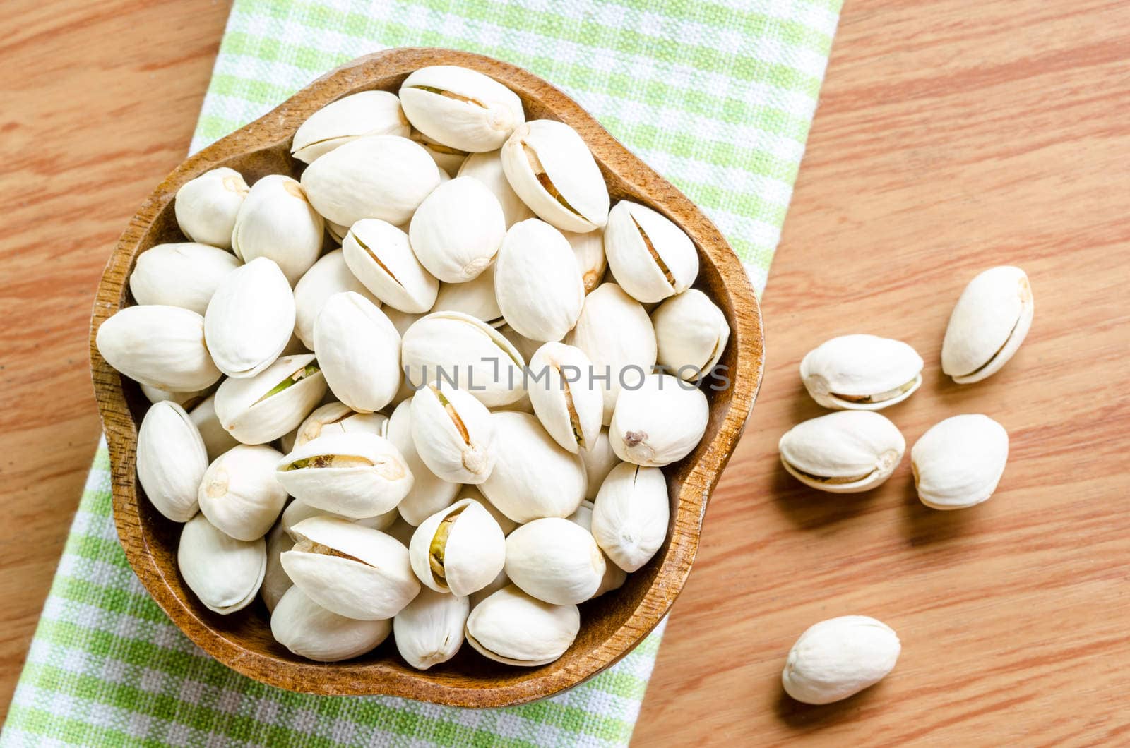 Pistachio nuts in wooden bowl on tablecloth and wooden background.