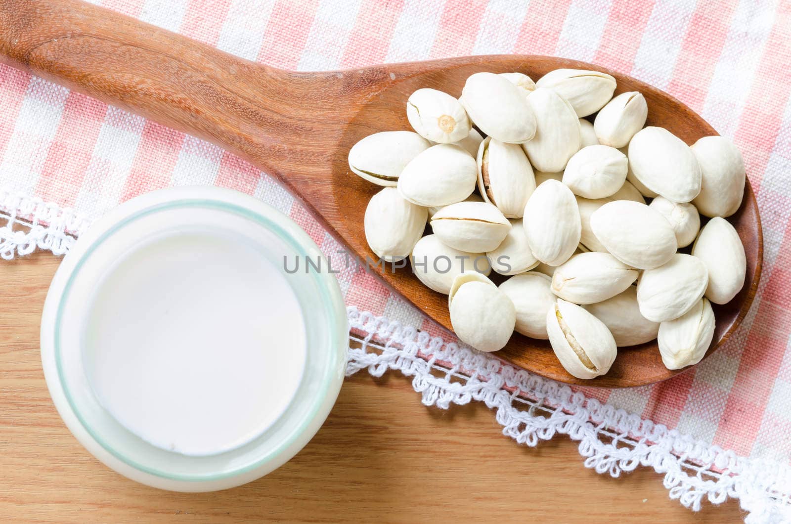 Pistachio in wooden spoon with milk in glass on tablecloth background.