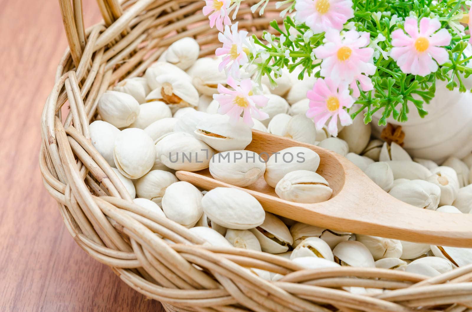Pistachio nuts in wood basket and woo spoon with flower on wood background.