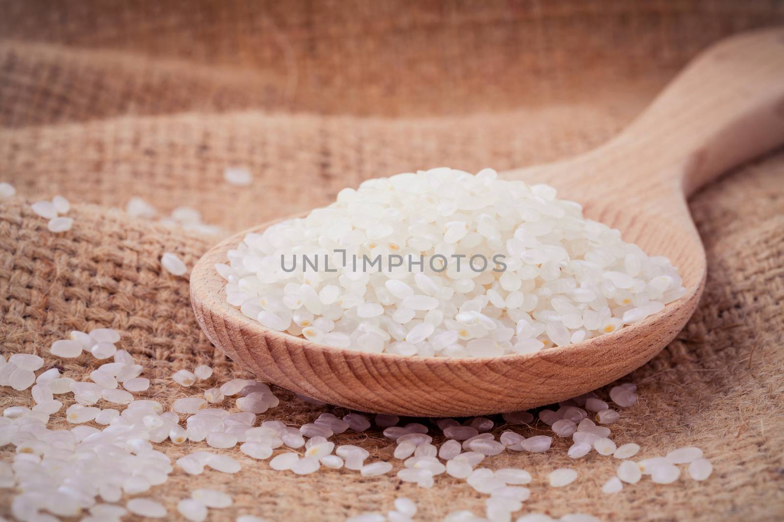 Whole grain traditional japanese rice  in wooden spoon with hemp sacks background