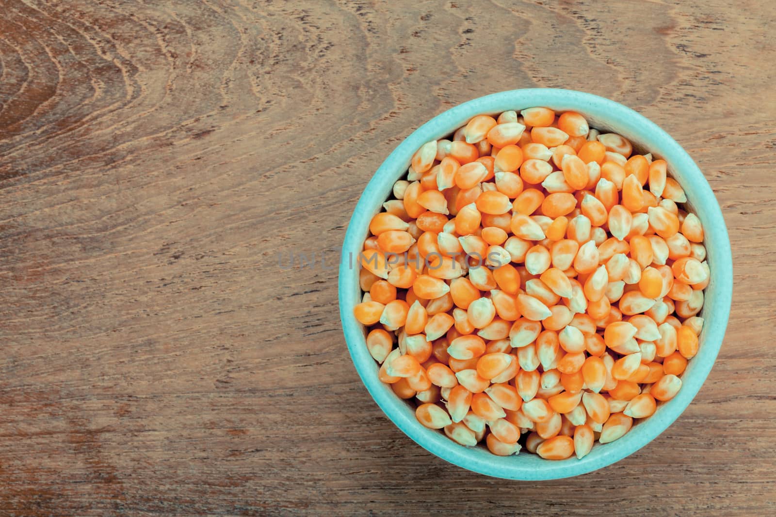 Grains of ripe corn in the bowl on teak wood background .