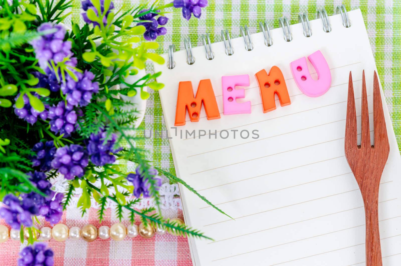 Open diary and wooden spoon fork with flower on beautiful fabric background. Menu concept.