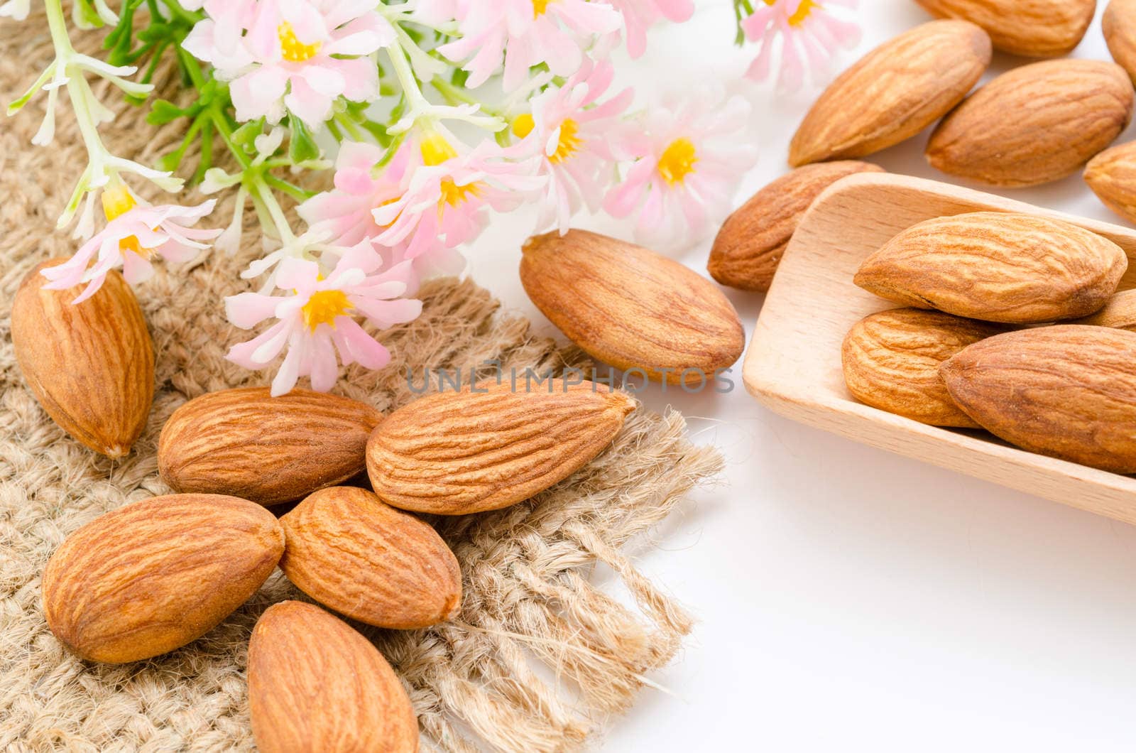 Almonds in wooden spoon with flower on white background.