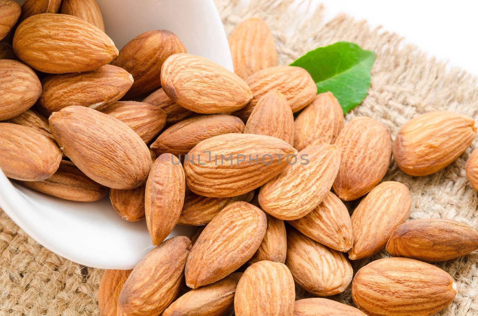 Almonds in white bowl with green leaf on sack background.