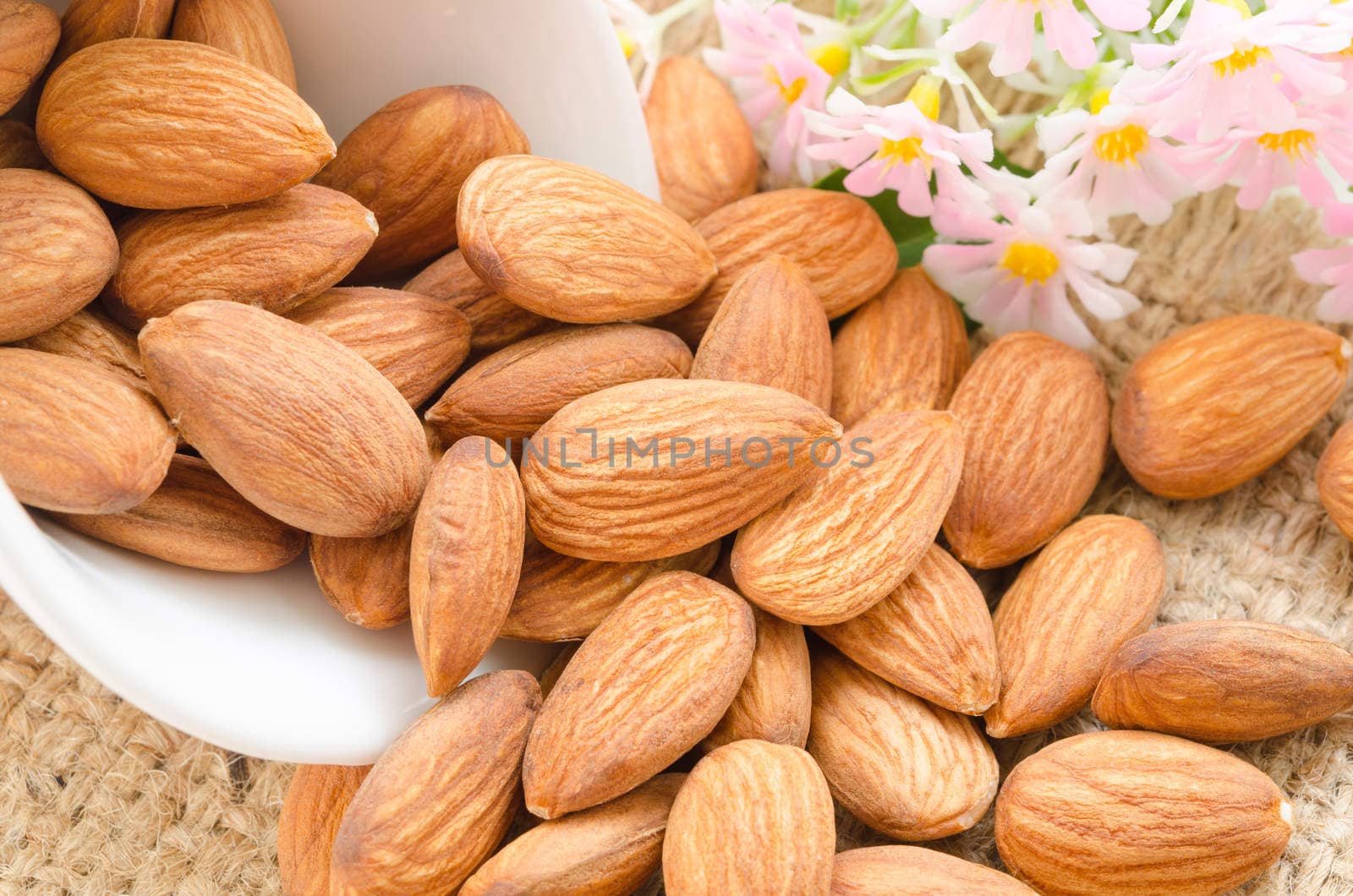 Sweet almonds in white cup with flower on sack background.