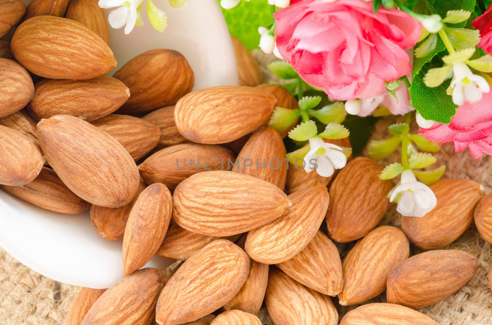 Almonds in white cup with pink flower on sack background.