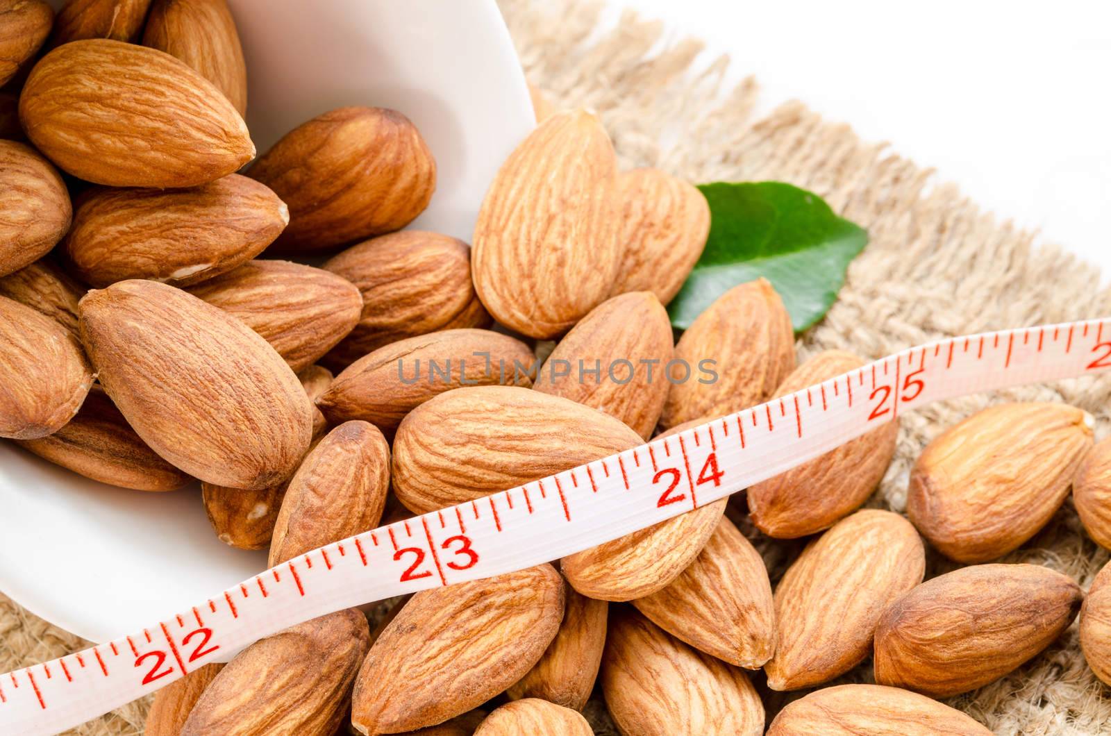 Almond and measuring meter with green leaf on sack background. Diet concept.