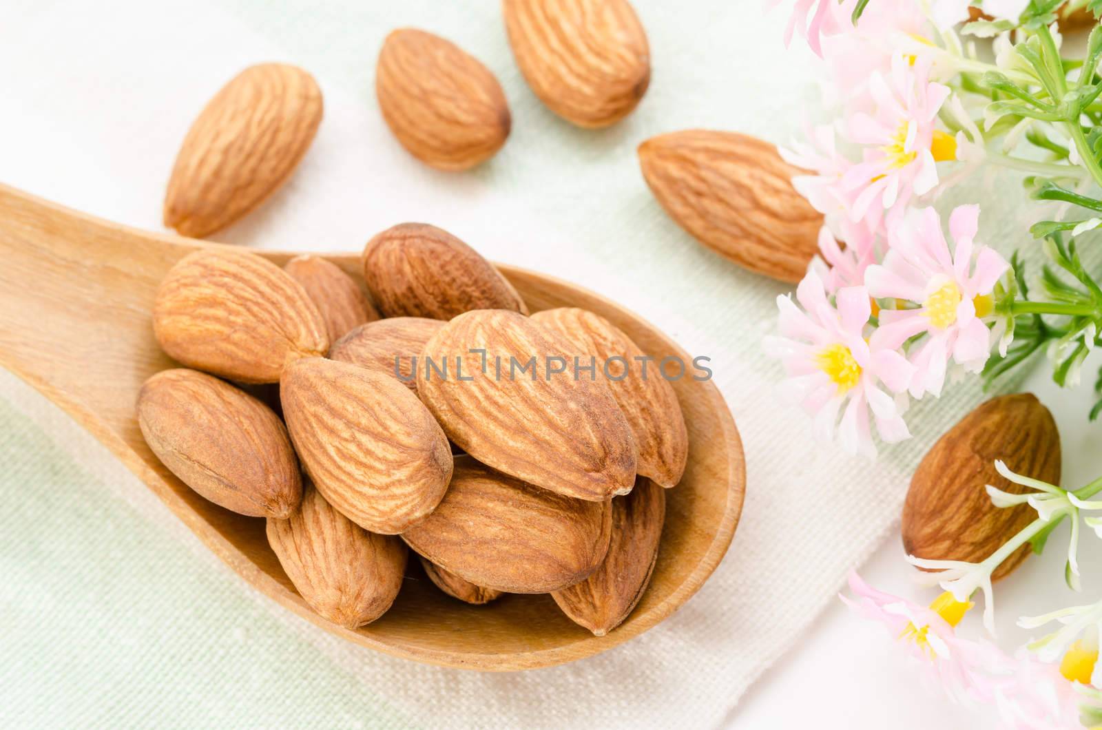 Almonds in wooden spoon with flower on tablecloth background.