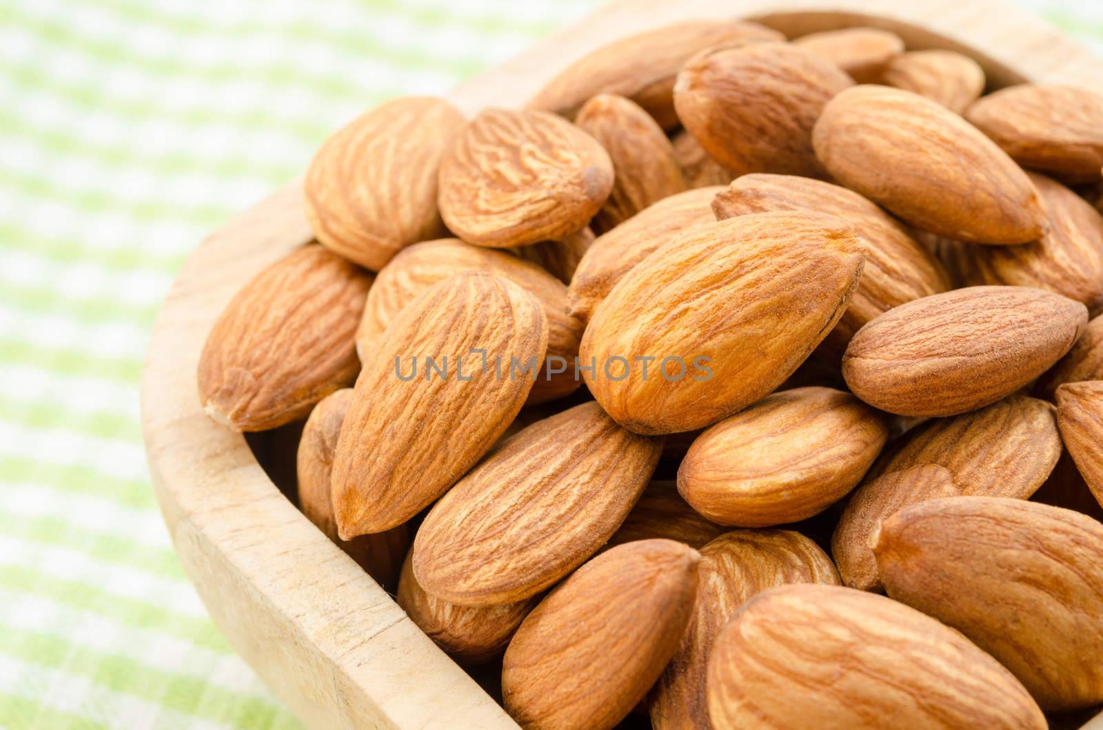 Almonds in wooden cup on green tablecloth.