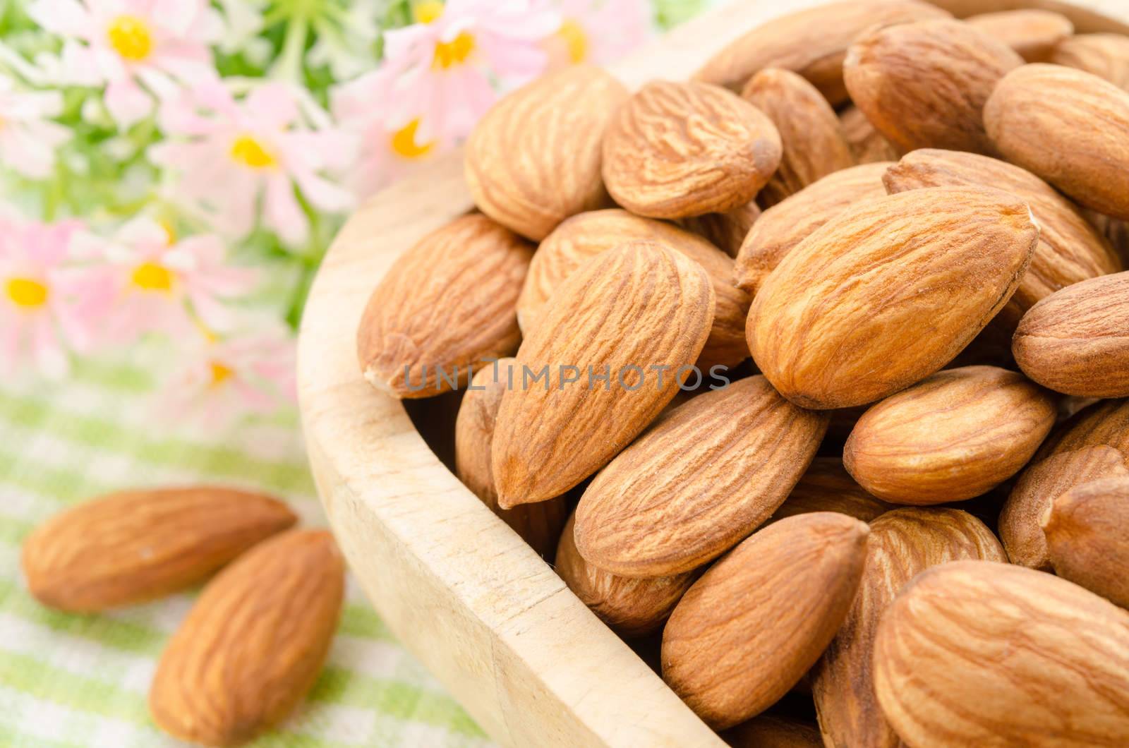 Almond in wooden cup with flower on fabric background.