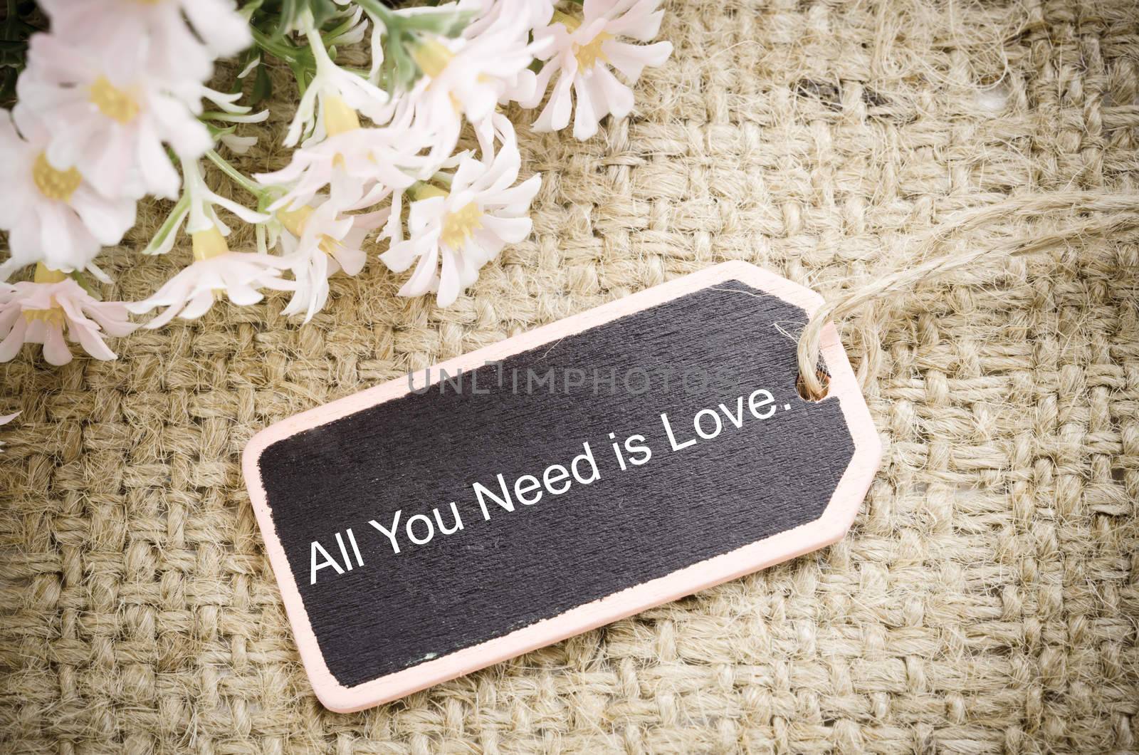 All you need is love vintage wood tag with flower on sack background.