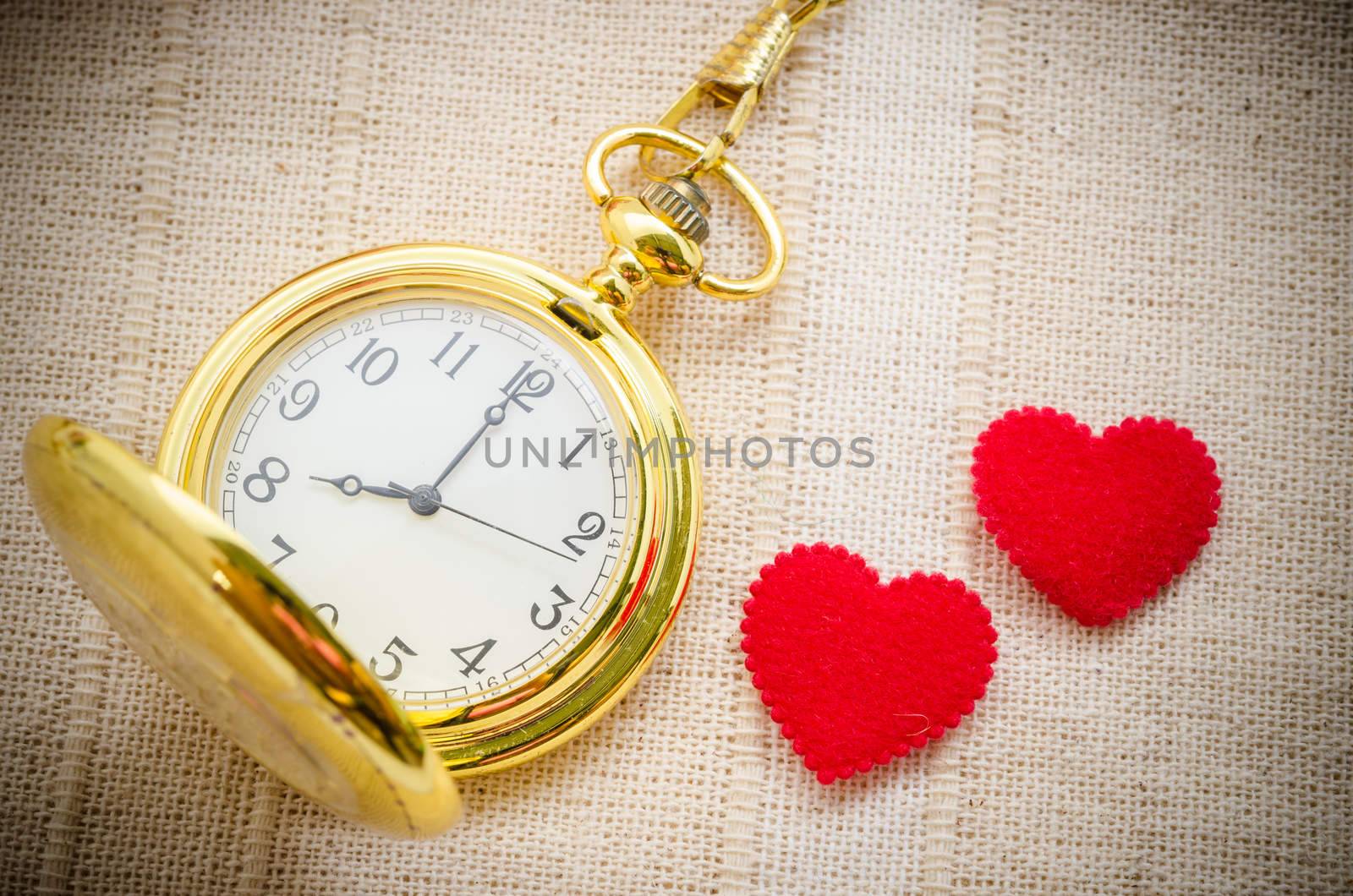 Gold pocket watch and red heart on sack background. Love concept.