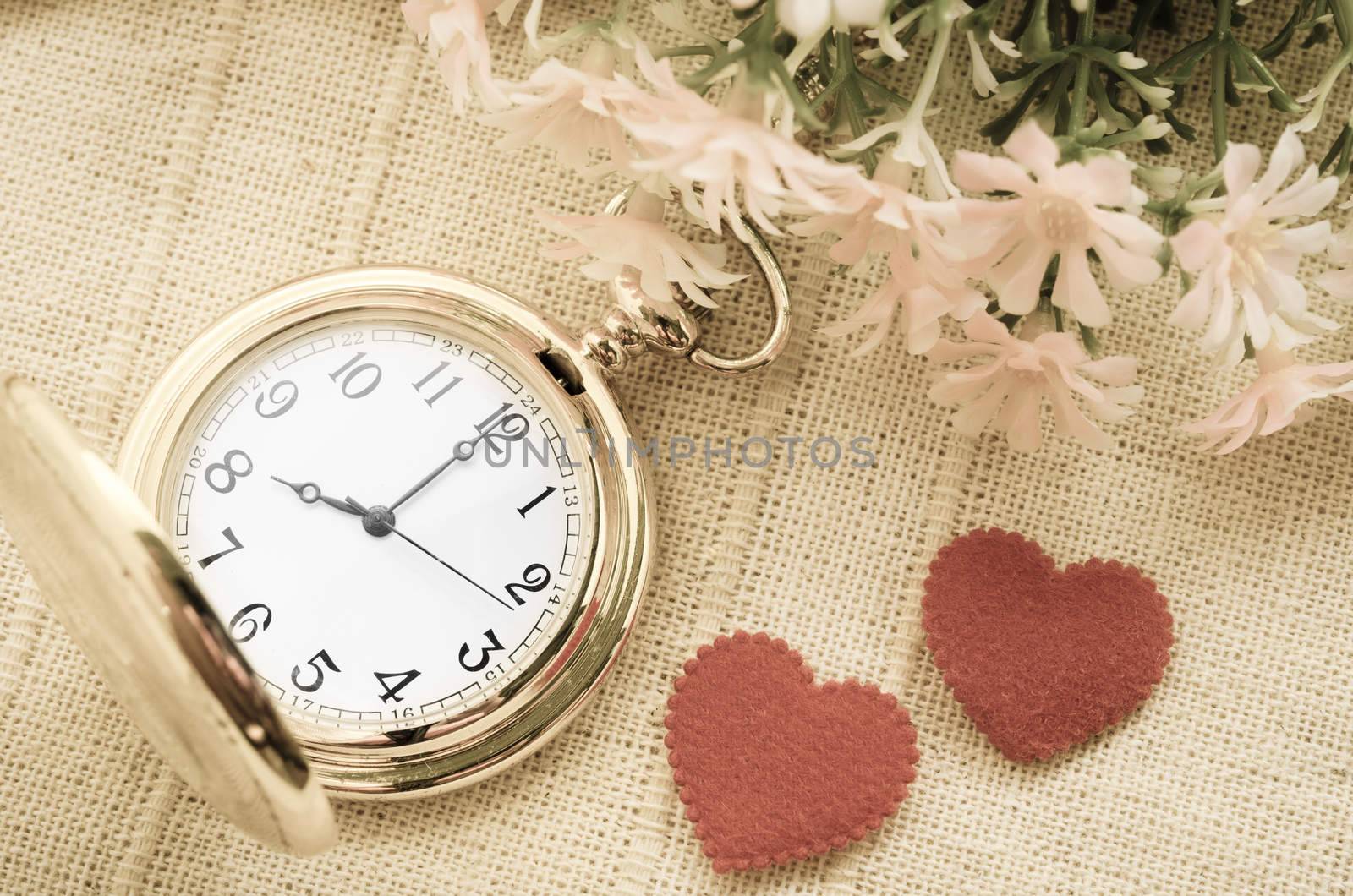 Gold pocket watch and red heart with flower on sack background. Love concept.