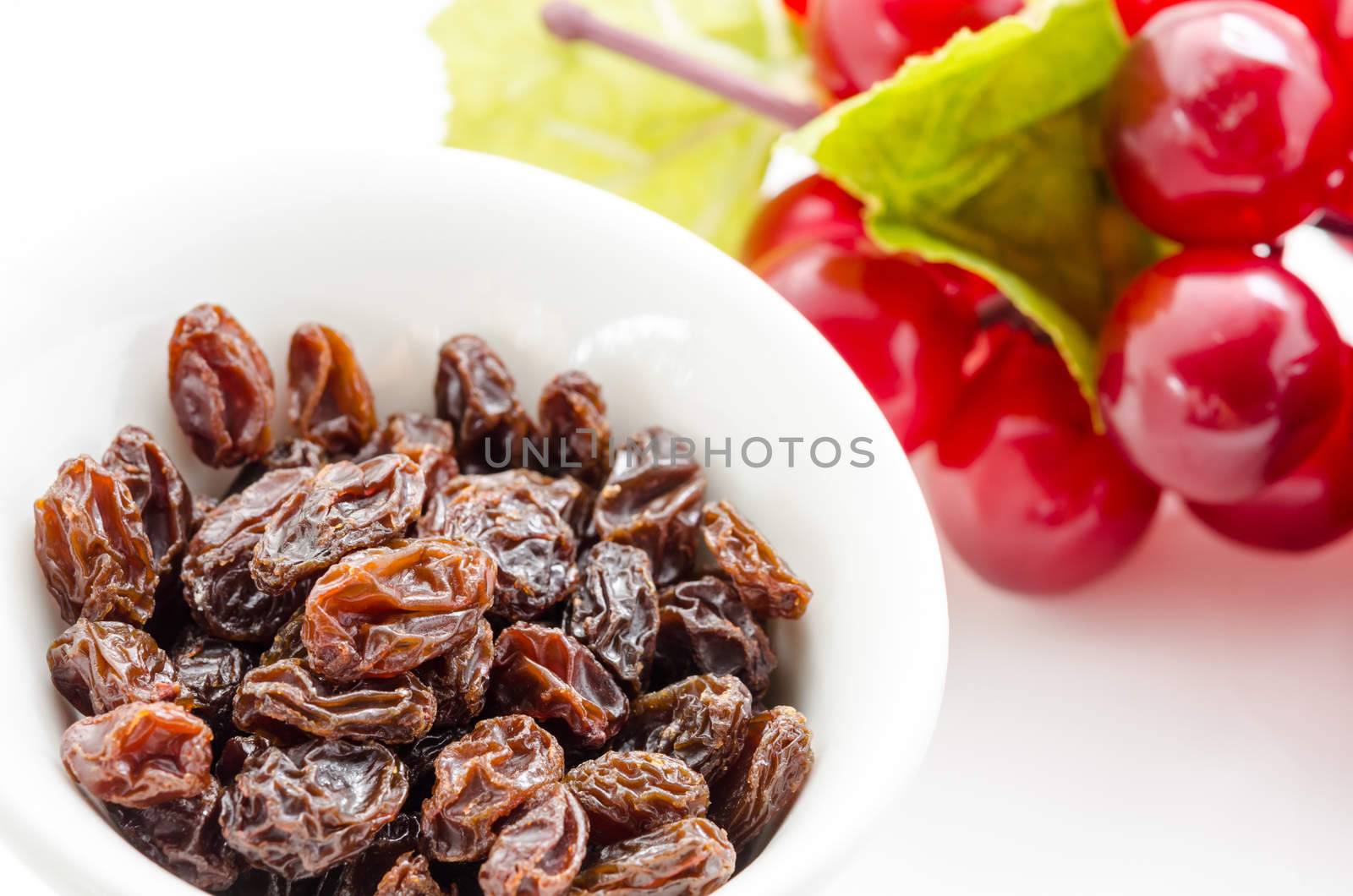 Raisins in bowl with red grapes on white background close up