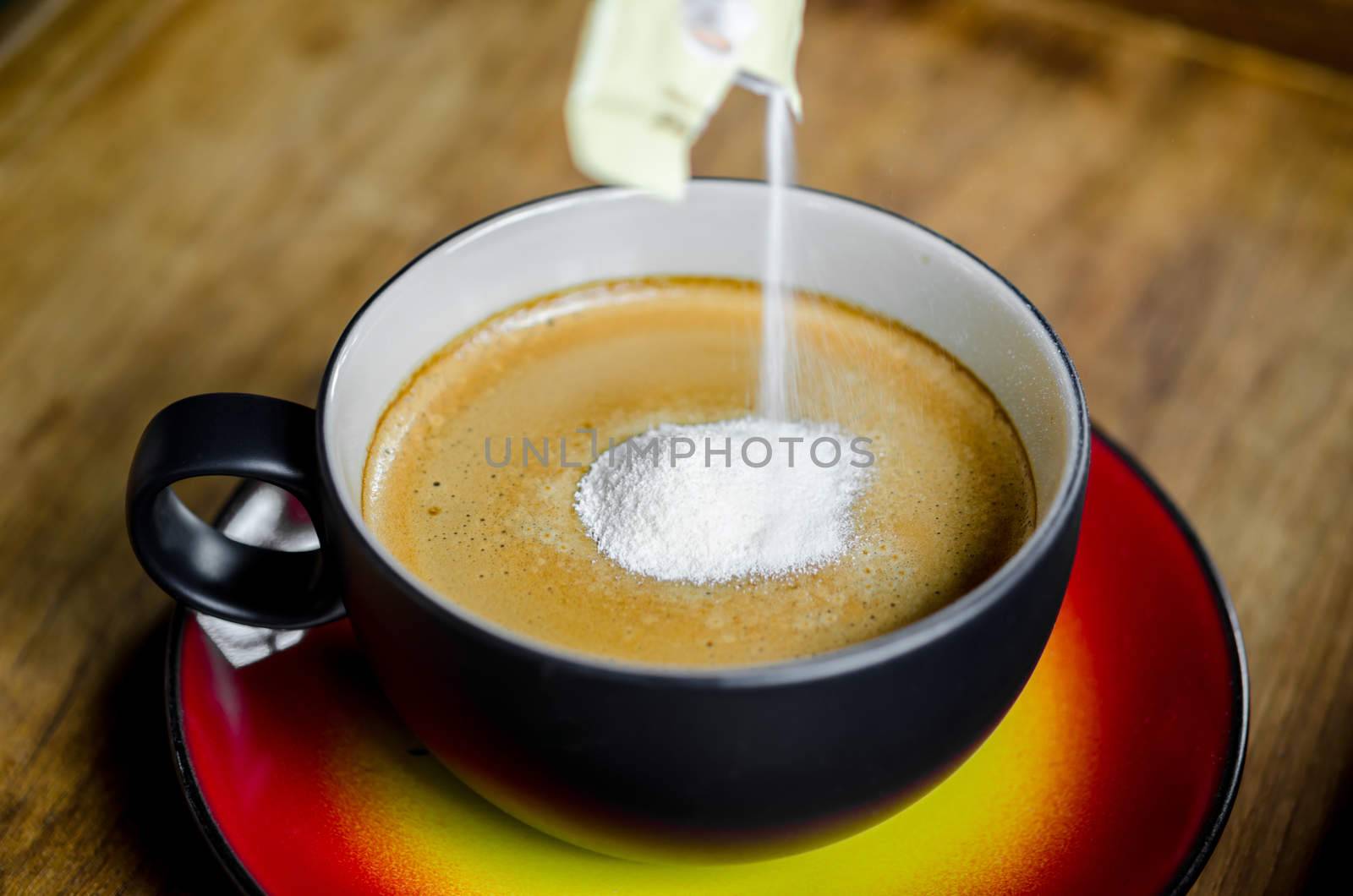 Hand pouring creamer in to a cup of coffee on wooden background.