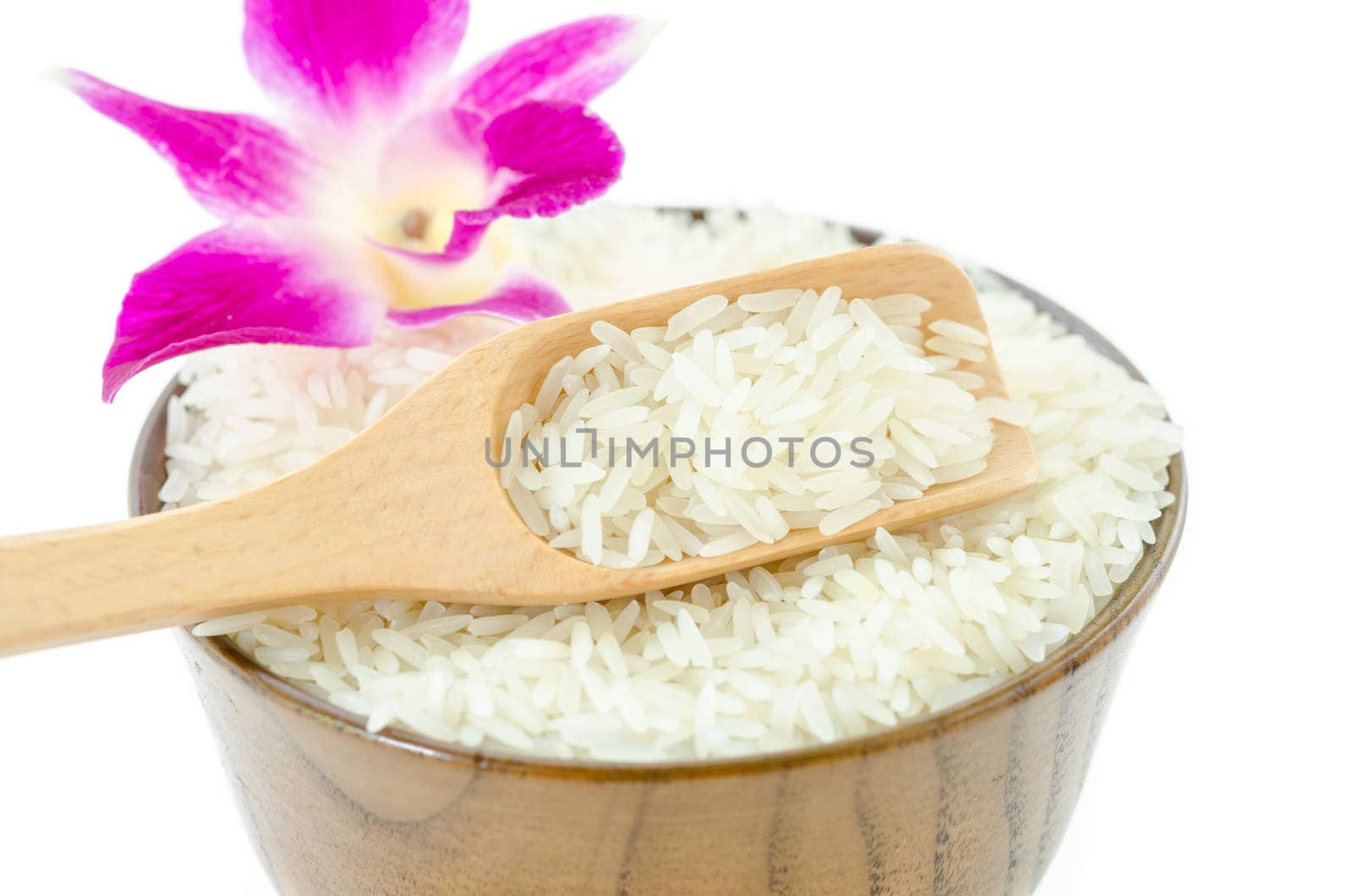 Jasmine rice in wooden spoon and vioelt orchid on white background.