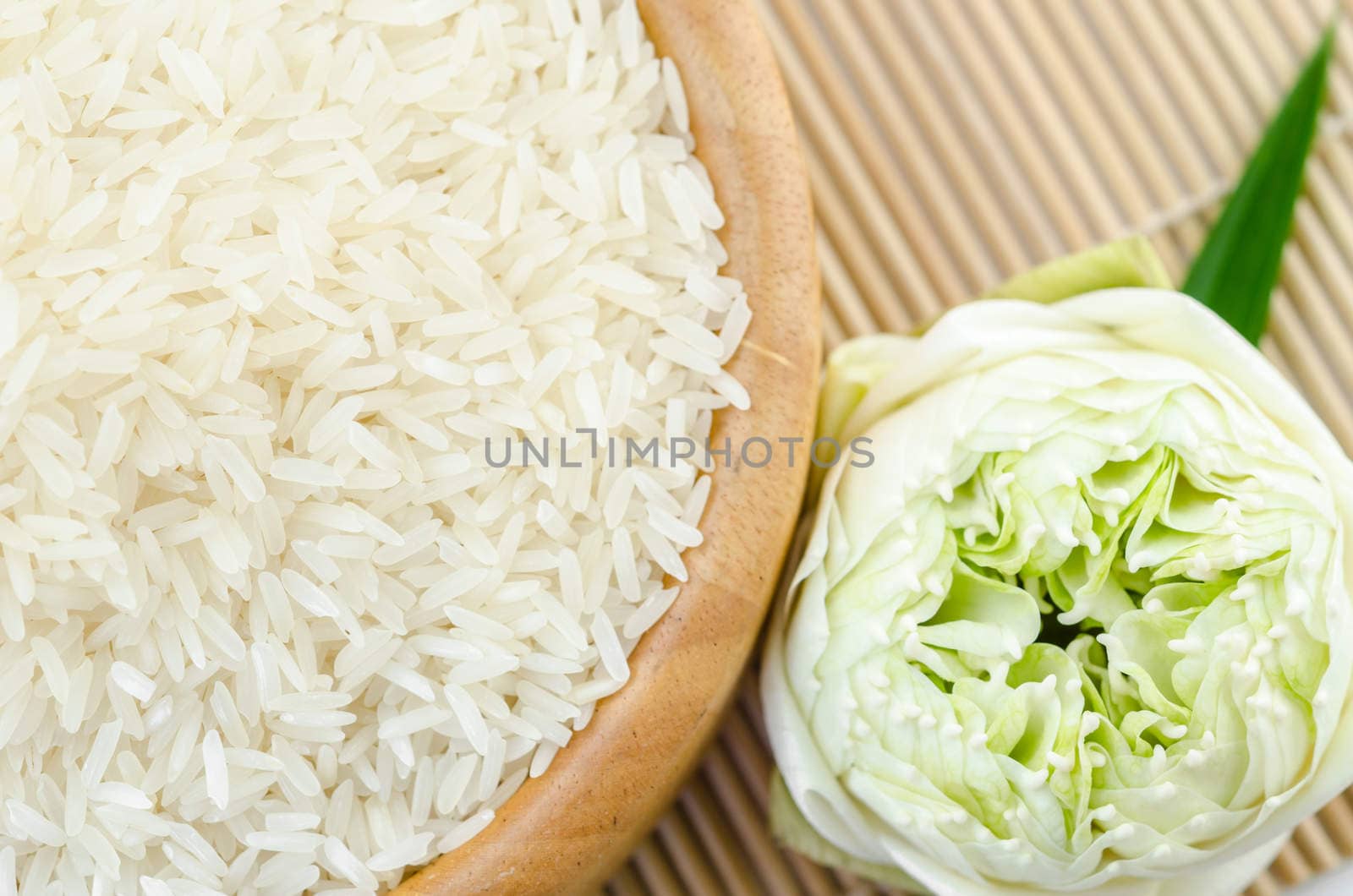 Raw rice jasmine on wooden bowl with lotus flower on bamboo mat background.