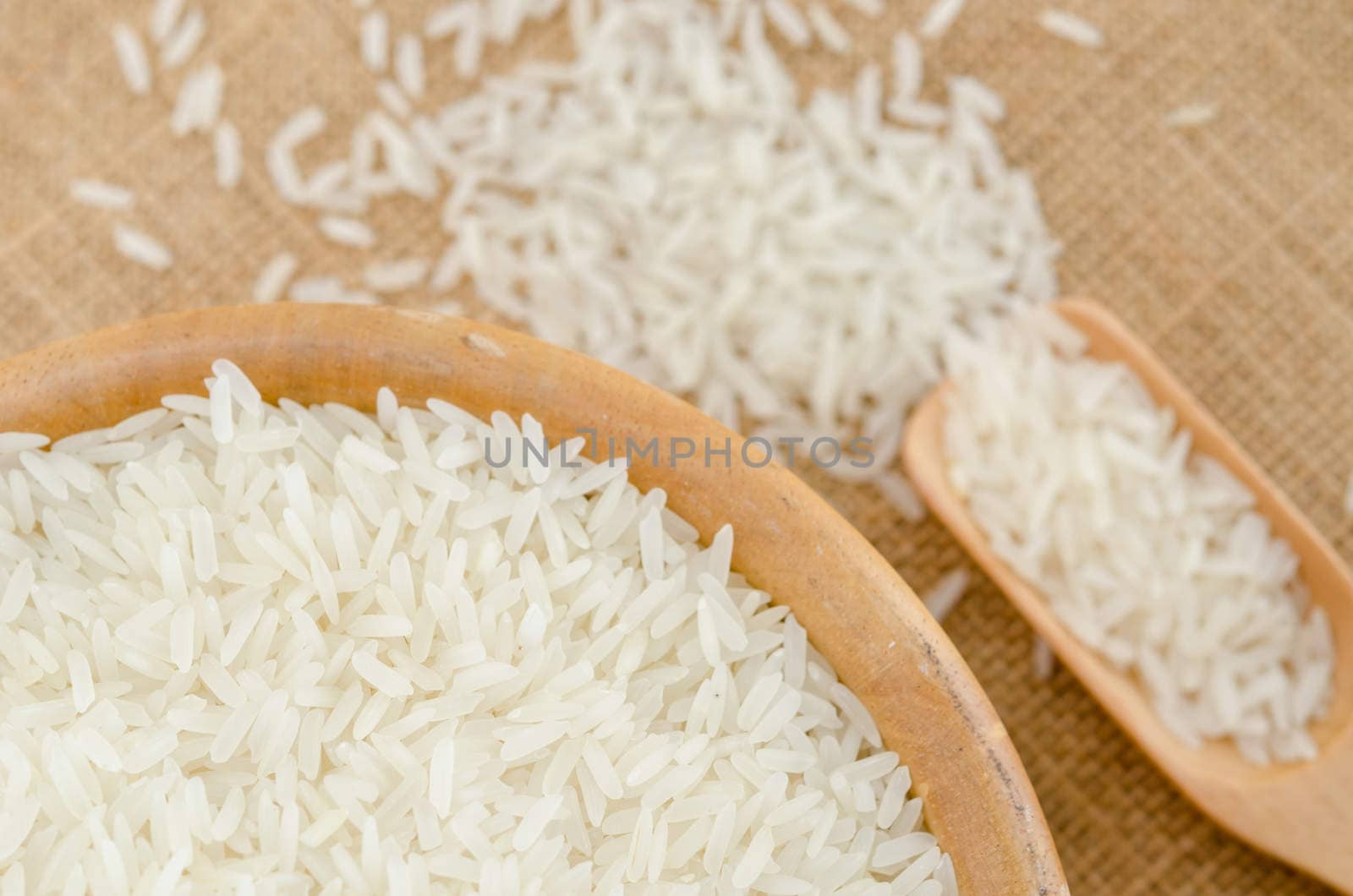 Raw rice in wooden bowl on sack background.