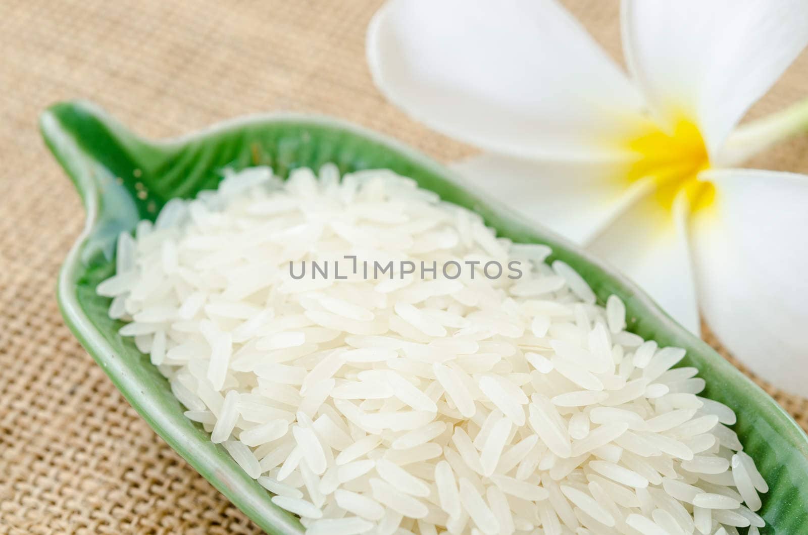 Raw white rice in green cup with flower on sack background.