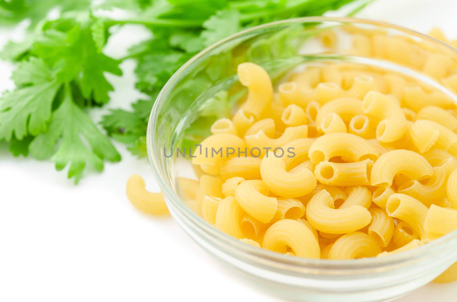Raw dry elbow macaroni pasta in glass cup and coriander on white background.