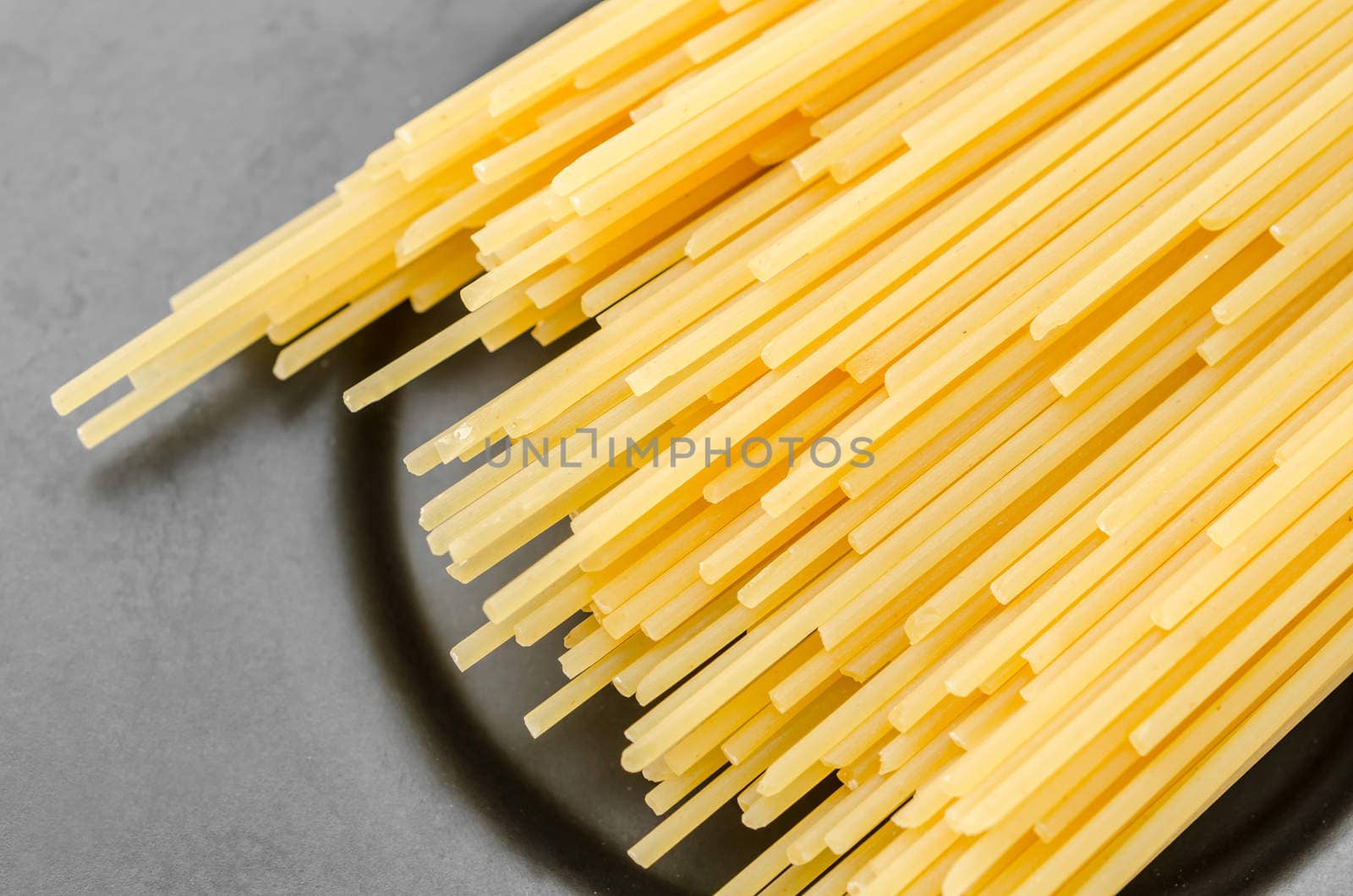 Uncooked pasta spaghetti macaroni on black dish background.